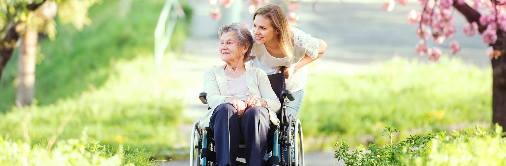 Betreuungskraft schiebt eine alte Dame im Rollstuhl